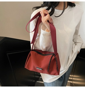 Gros plan sur le sac bandoulière en toile rouge avec logo et détail de fermeture tissé