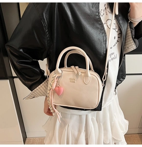 Détail d'un mini sac Boston beige avec breloque coeur et bandoulière tissée sur tenue