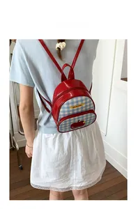 Vista dettagliata del mini zaino a scacchi con motivo a mela e scritta Not Anxious