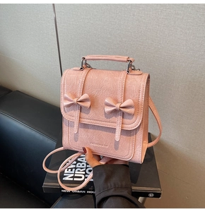 Detailed shot of pink mini backpack with textured leather and dual bow decorations