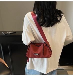 Détail du sac bandoulière bordeaux en toile avec sangle large et logo noir chic