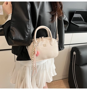 Détail du sac bandoulière crème en PU avec logo et pompon cœur porté par le mannequin