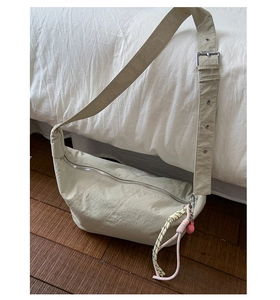 Detail of cream nylon crescent crossbody bag with braided rope charm and silver hardware