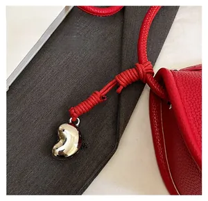Détail d'un sac à main rouge en cuir grainé avec un pendentif en métal argenté poli