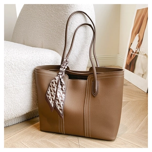 Detail of brown leather tote bag with contrast stitching and decorative silk scarf