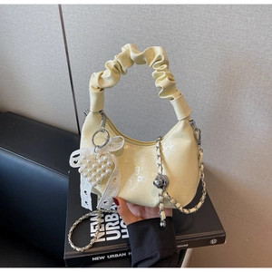 Detail of creamy yellow crescent bag featuring ruffled handle and pearl heart charm