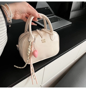 Détail d'un sac à main beige en similicuir avec logo FAN TOR et breloque cœur au bureau