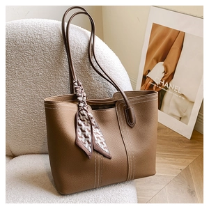 Detailed view of a brown leather tote bag with white stitching and a silk scarf on a sofa
