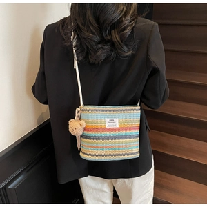 Detail of colorful striped crochet bucket bag featuring a plush bear charm and brand label