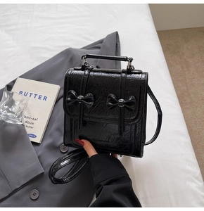 Detail of a black shiny backpack with bows placed on a grey blazer and book