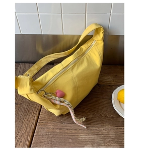Detail of yellow nylon dumpling bag with knotted strap and pink heart charm on wooden surface
