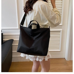 Close-up of a large black nylon tote bag with wide strap worn by a model in a room