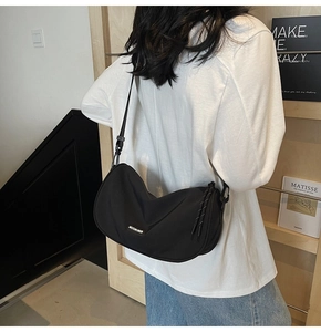 Minimalist black crescent shoulder bag with silver logo worn by model in a modern room