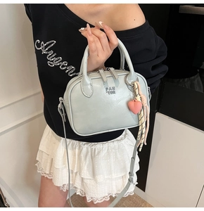 Détail du sac bandoulière bleu clair avec logo doré et breloque coeur sur fond minimal