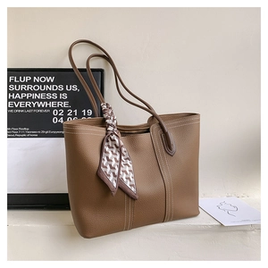 Close-up of brown pebbled leather tote bag featuring white stitching and silk scarf detail