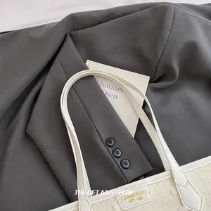 Detailopname van de witte lederen handvatten en de gouden logoplaat op de tote bag