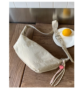 Detail of beige nylon crescent bag with wide adjustable strap and heart pendant