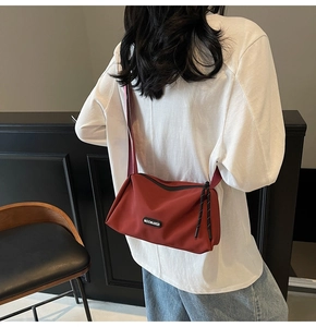 Détail d'un sac bandoulière en nylon bordeaux avec large sangle porté par un mannequin