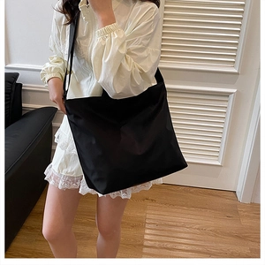 Detailed view of a black nylon tote bag with wide strap on a model in a minimalist room