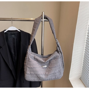 Detail of grey puffer tote bag with wavy quilted nylon texture and silver metal brand plate