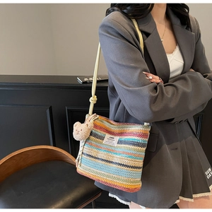Detail of woven straw bucket bag with rainbow stripes and a brown plush bear charm
