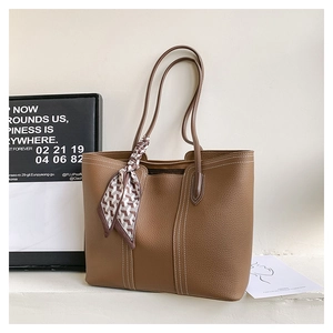 Macro shot of brown lychee leather tote bag with white stitching and decorative scarf