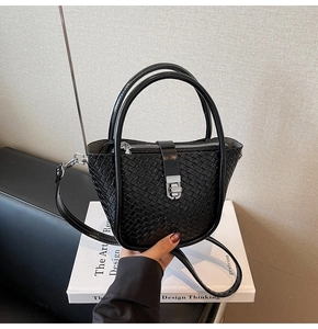 Detail shot of black woven texture leather bucket bag with silver metal buckle on a book