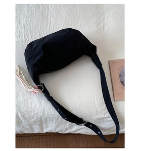 Detail view of black crescent crossbody bag with woven pendant and adjustable strap