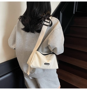 Détail d'un sac bandoulière en toile crème avec large sangle porté par un mannequin