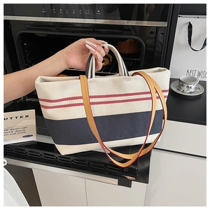 Detailansicht der cremefarbenen Canvas-Tasche mit rot-blauen Streifen und Ledergriff