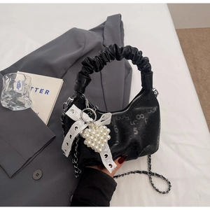 Close-up of ruched handle, silver chain, and heart pearl charm on black leather bag