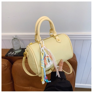 Close-up of yellow lychee leather boston bag with rainbow charms and gold hardware detail