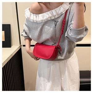 Détail d'un sac selle rouge avec bandoulière tressée et breloque coeur sur modèle