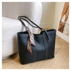 Close-up of black pebble leather tote bag with white stitching and decorative silk scarf