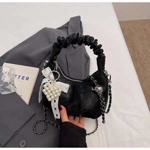 Detail of black textured leather bag with white lace bow and pearl heart pendant