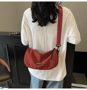 Detailed view of a red nylon crescent crossbody bag with a wide strap on a model