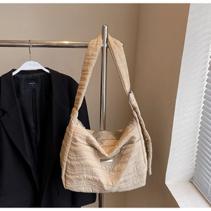 Close-up of beige quilted tote bag featuring soft pleated texture and silver logo plate