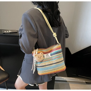 Close-up of a colorful striped woven bucket bag with a cute bear charm and knotted strap