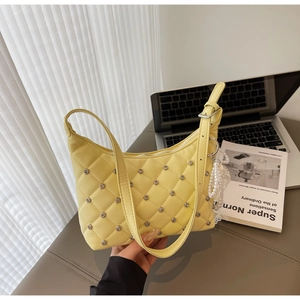 Detail of light yellow quilted shoulder bag with silver studs and pearl lace charm