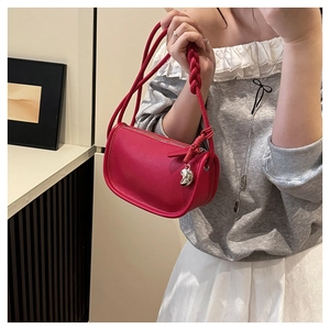 Détail du sac selle en cuir grainé rouge avec poignée tressée et pendentif coeur