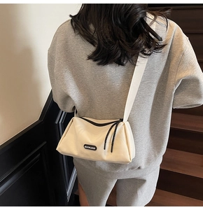 Détail d'un sac bandoulière à large sangle montrant le logo et le tissu texturé