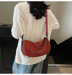 Close-up of red crescent shoulder bag with adjustable strap and brand logo on model