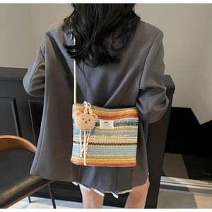 Detail of colorful striped woven straw shoulder bag with plush bear charm and woven strap