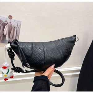 Detail of black textured leather croissant bag with layers and duck charm accessory