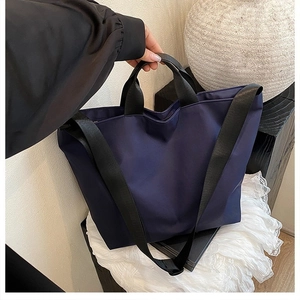 Detail of navy blue nylon tote bag with black handles and woven shoulder strap
