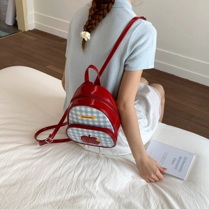 Dettaglio mini zaino rosso lucido con patch mela a scacchi ed etichetta gialla