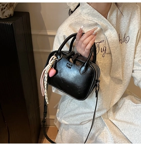 Détail d'un sac bandoulière noir avec breloque cœur rose et logo Pan Tor gravé