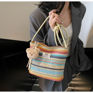 Detail of colorful striped woven bucket bag featuring a cute plush bear pendant accessory