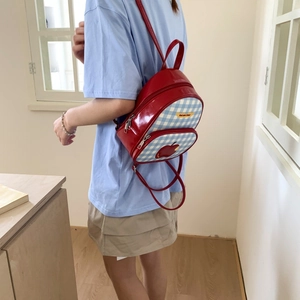 Dettaglio mini zaino in pelle verniciata rossa con motivo a scacchi blu e patch mela