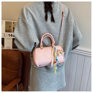 Pink litchi texture boston bag with rainbow charm and crossbody strap on leather sofa